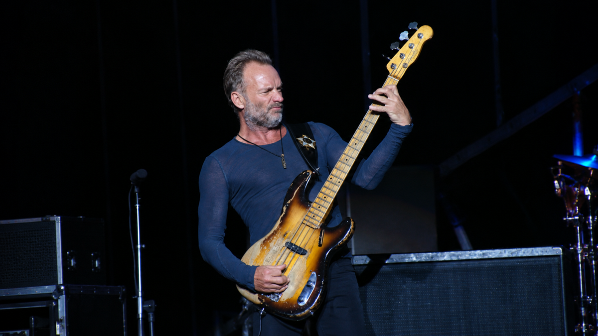 Sting performing on stage while playing a worn electric bass guitar.