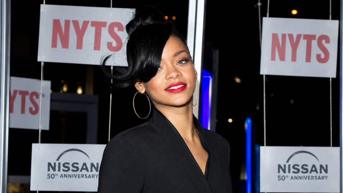Rihanna posing in front of a backdrop featuring “NYTS” and “Nissan 50th Anniversary” logos.