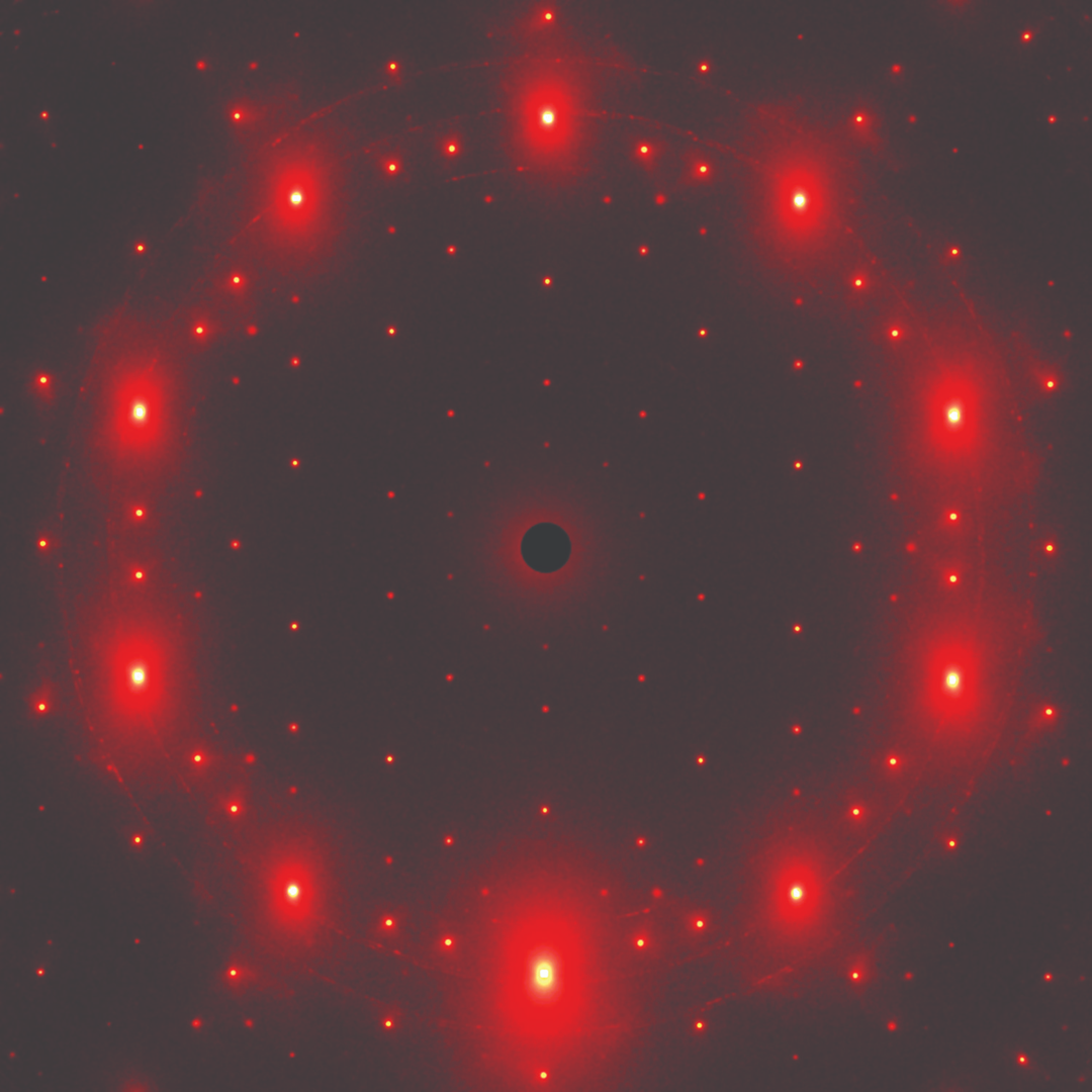 A diffraction pattern showing a circular arrangement of bright red spots on a dark background.