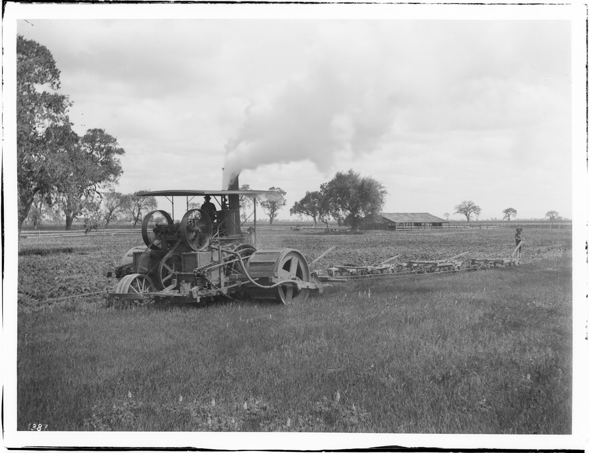 A steam-powered tractor pulling a plow across a large field.