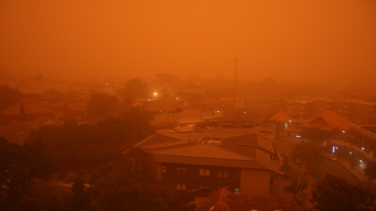 Weather events. A city neighborhood obscured by a thick orange haze from a dust storm or wildfire smoke.