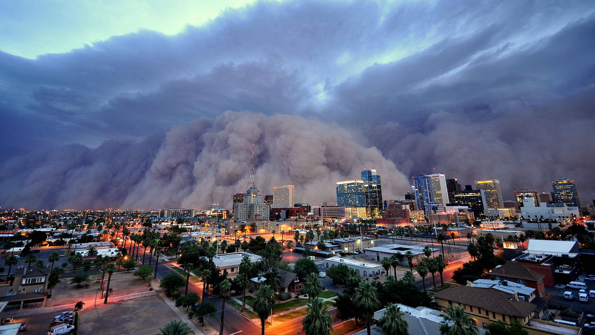 A massive dust storm looms over a city skyline at sunset.