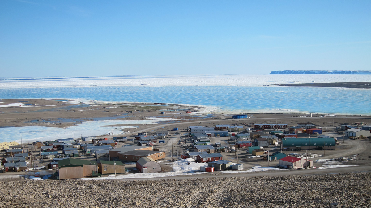 A coastal town with colorful houses and buildings situated along a bay filled with sea ice.
