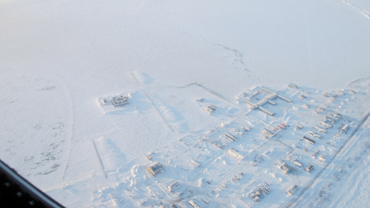 Aerial view of a small, snow-covered settlement surrounded by a vast, frozen icy landscape.
