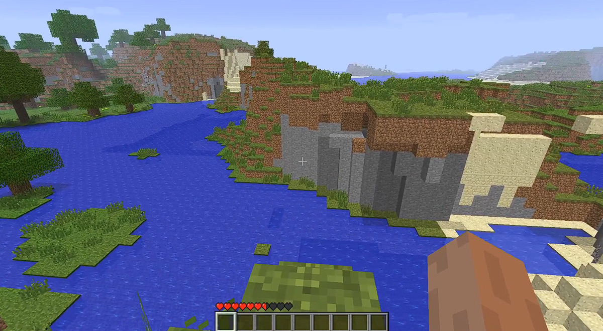 A first-person view of a Minecraft landscape with a body of water, grassy hills, and stone cliffs.