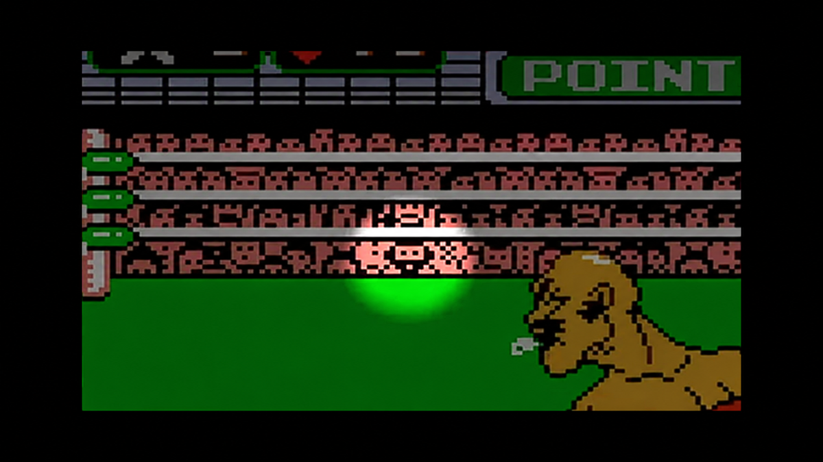 A pixel-art video game screen showing a crowd in the stands above a green ring, with a mustachioed man in the foreground.
