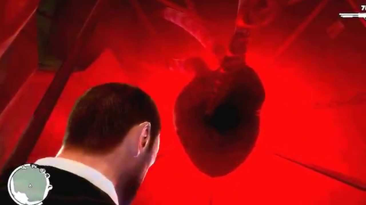 A person in a dark suit looking up at a large, pulsing heart suspended in a red-lit room.