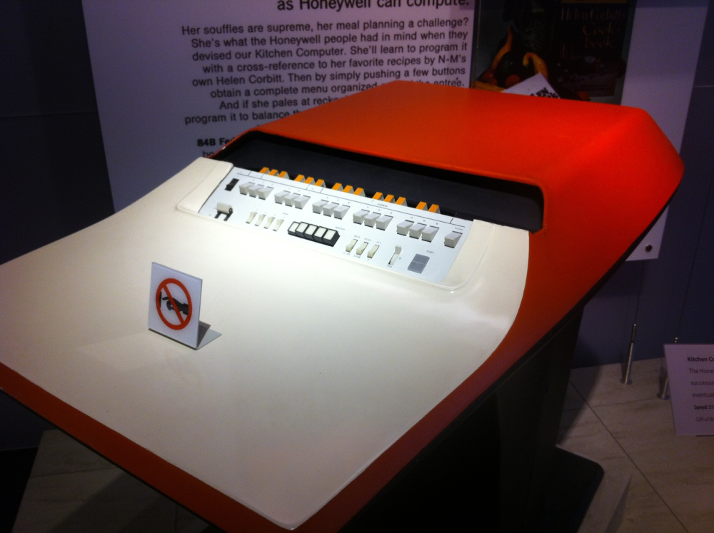A vintage orange and cream Honeywell Kitchen Computer console with a sign displaying a “do not touch” icon.