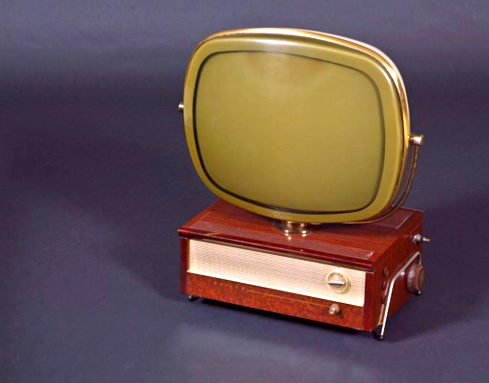 A vintage mid-century television set featuring a rounded, gold-rimmed screen mounted atop a rectangular wooden base with a speaker grille and control knobs.