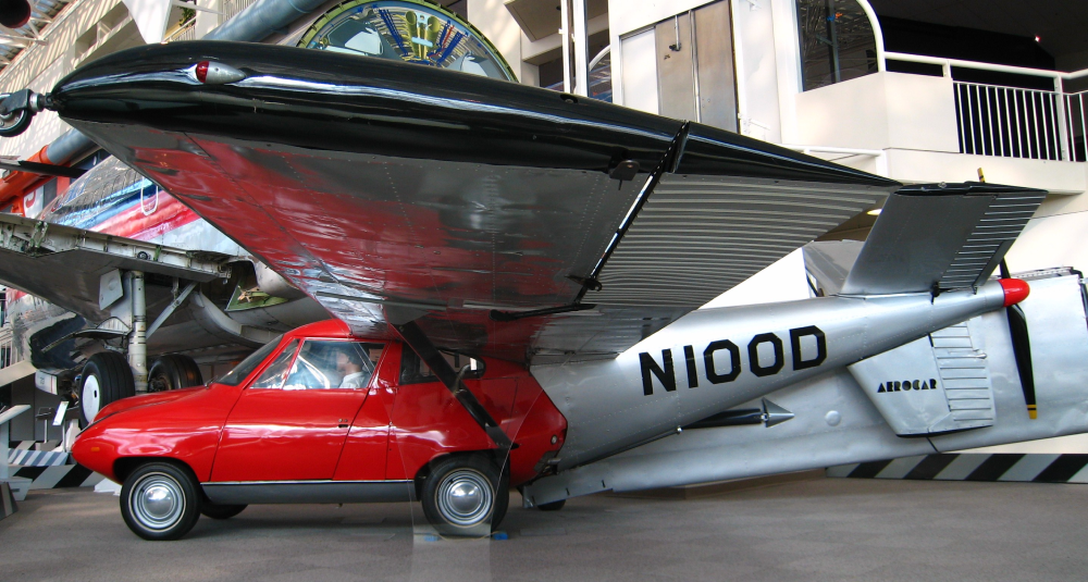 A red Aerocar flying car with silver wings parked inside a museum.