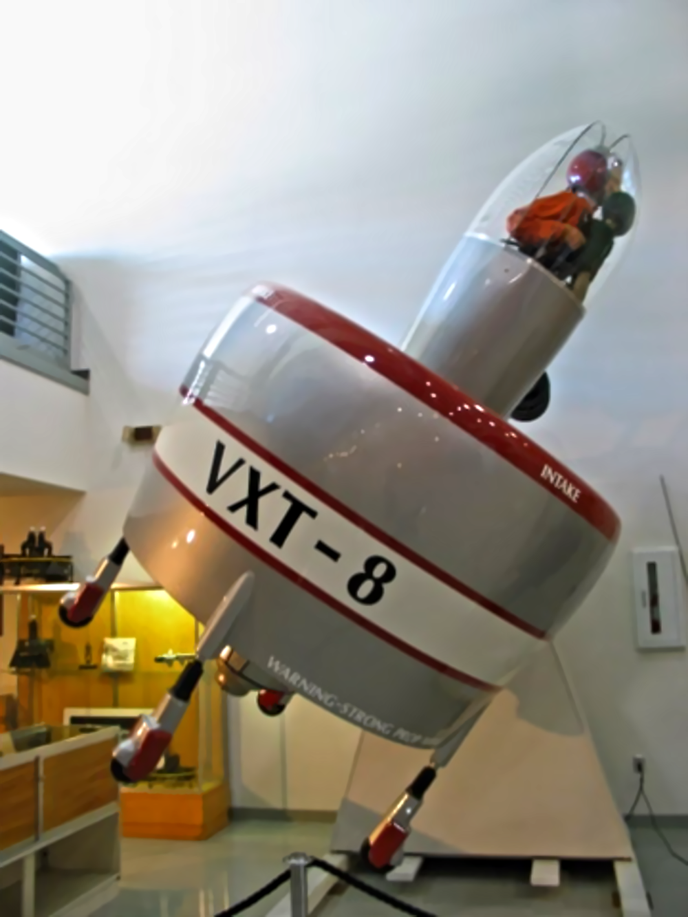 A vertical-takeoff aircraft display labeled “VXT-8” with a pilot visible inside the cockpit.