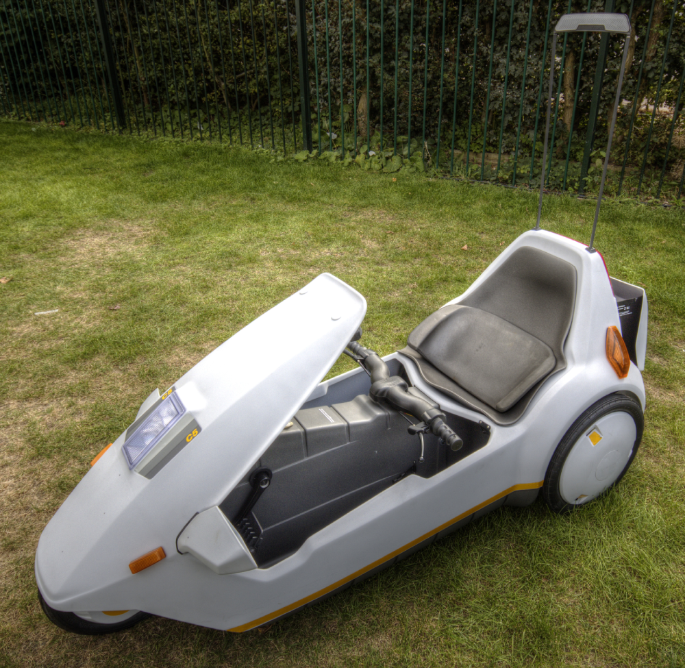 A white Sinclair C5 electric vehicle parked on a grass lawn.