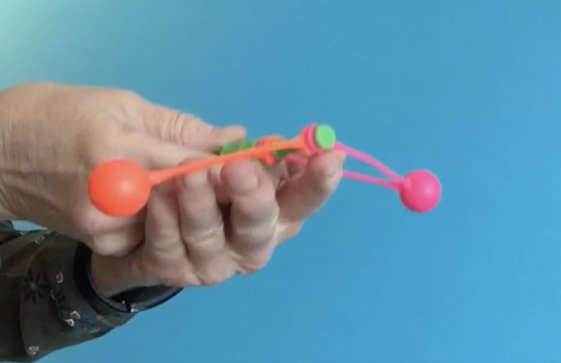 A hand holding a toy consisting of two colorful spheres connected by a central plastic mechanism.