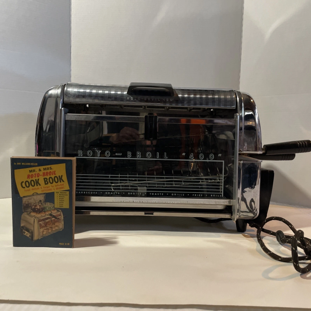 A vintage Roto-Broil 400 rotisserie oven next to its accompanying Mr. & Mrs. Roto-Broil cookbook.