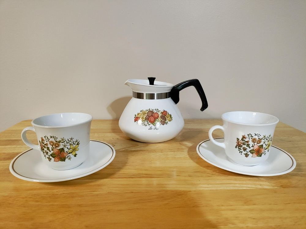 White teapot and two matching teacups on saucers, all decorated with colorful floral and fruit patterns.