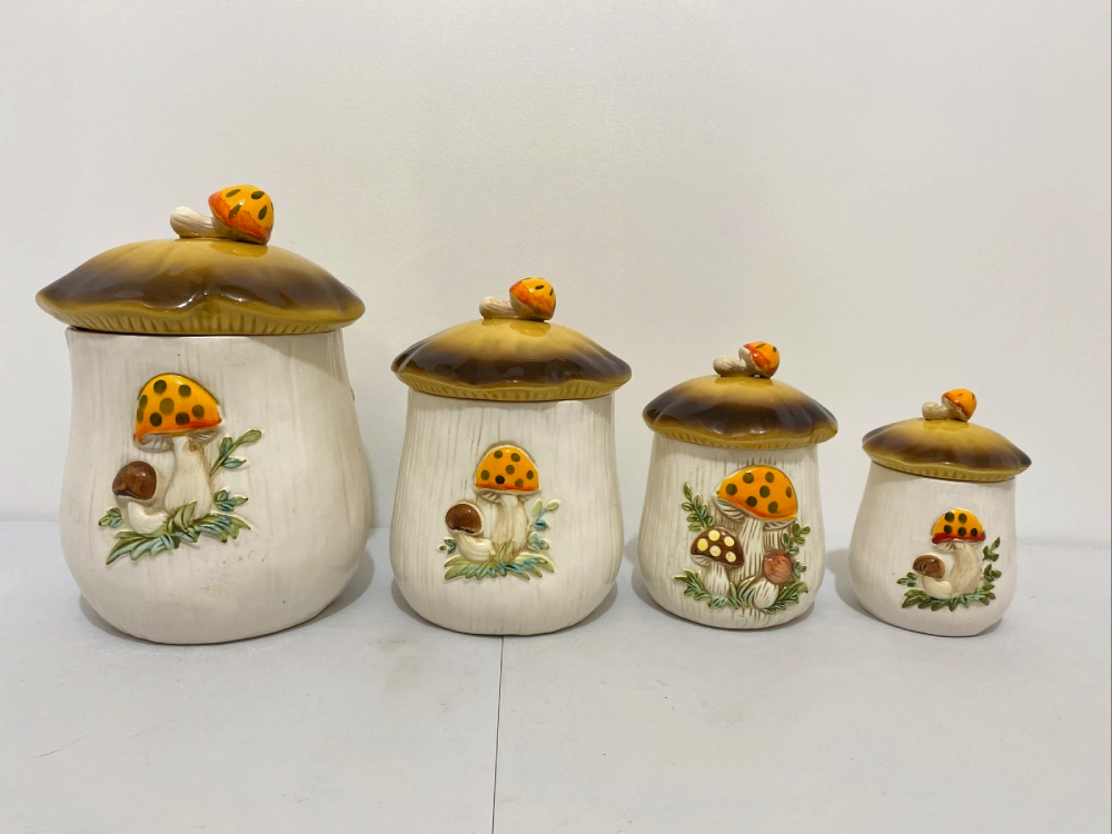 Four mushroom-shaped ceramic canisters of decreasing size, each featuring a brown cap lid topped with a small mushroom and decorative painted mushrooms on the base.