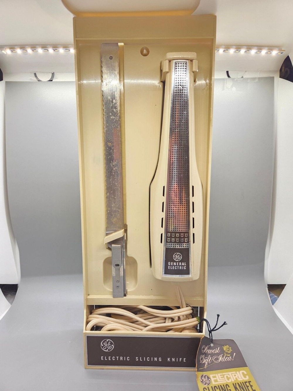 Vintage General Electric electric carving knife with a serrated blade and handle in its original plastic storage case, with a cardboard gift tag attached.