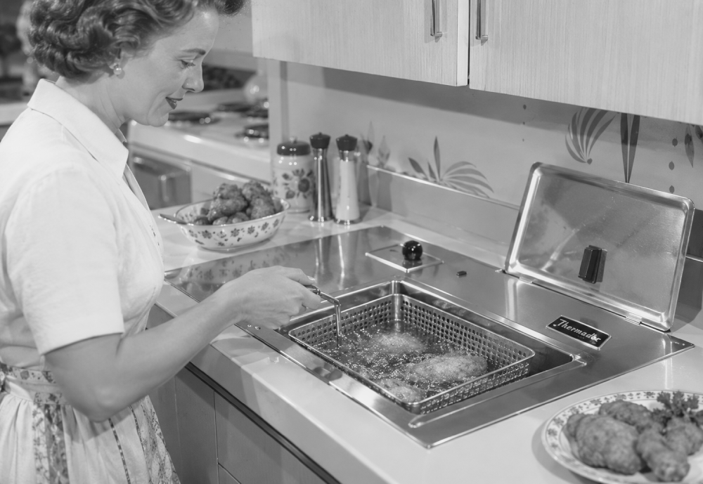 A woman in a kitchen uses a built-in electric deep fryer to cook food in oil.