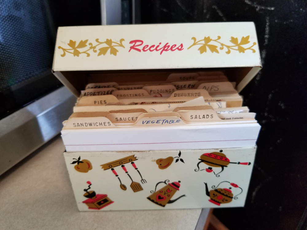 A vintage metal recipe box containing tabbed index cards with handwritten categories including Sandwiches, Sauces, Vegetable, and Salads.