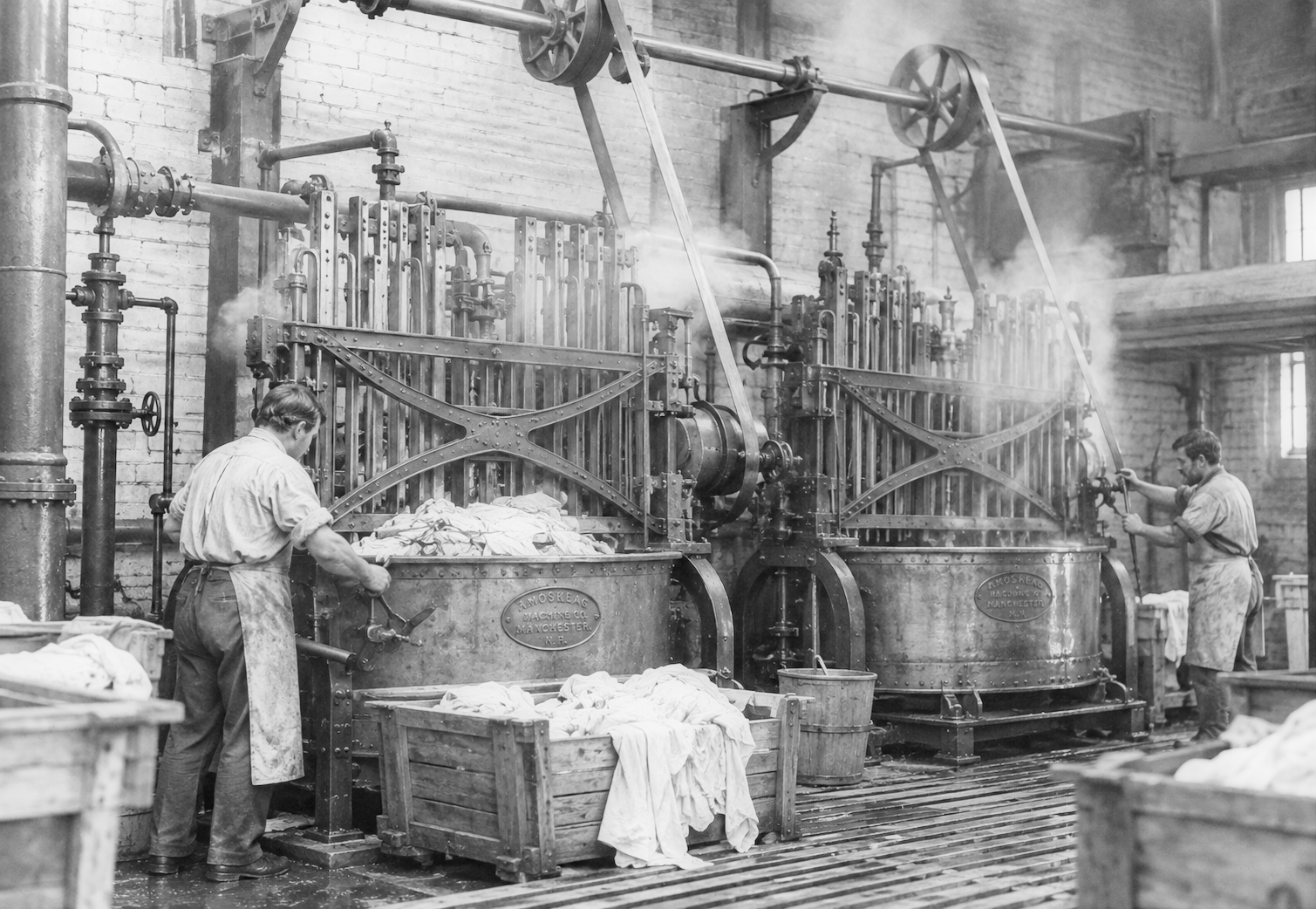 Two men work at large industrial washing machines in a factory, handling piles of fabric with steam rising from the equipment.