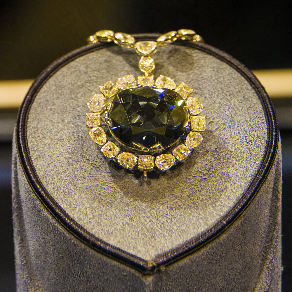 A large, dark blue diamond pendant surrounded by a halo of smaller white diamonds on a display stand.