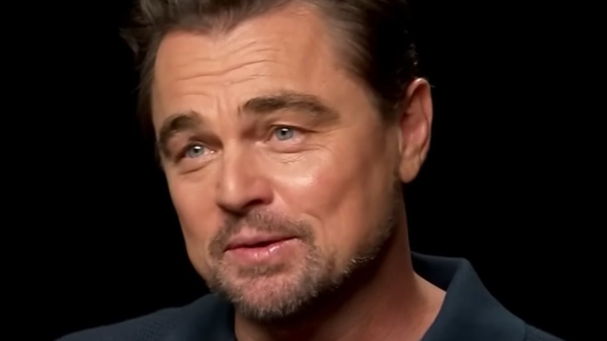 A man with light eyes, short brown hair, and a trimmed beard is smiling softly. He is wearing a dark collared shirt and is set against a black background.