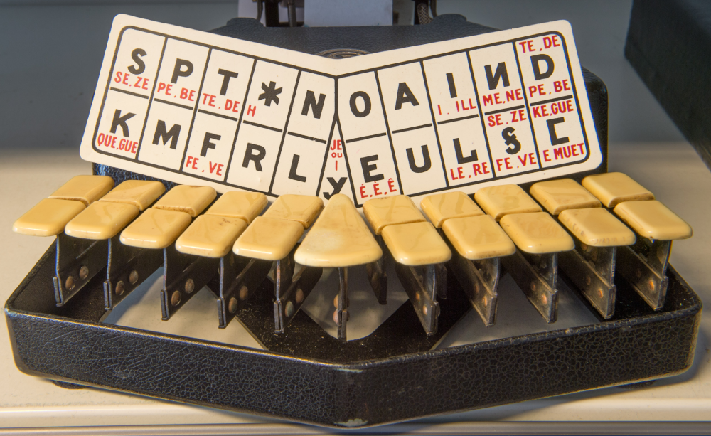 Close-up of a stenotype machine keyboard with a labeled letter layout plate above the keys.
