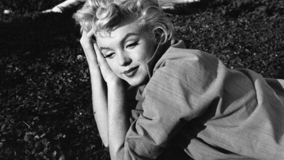 Marilyn Monroe lying in the grass, resting her head on her hand.