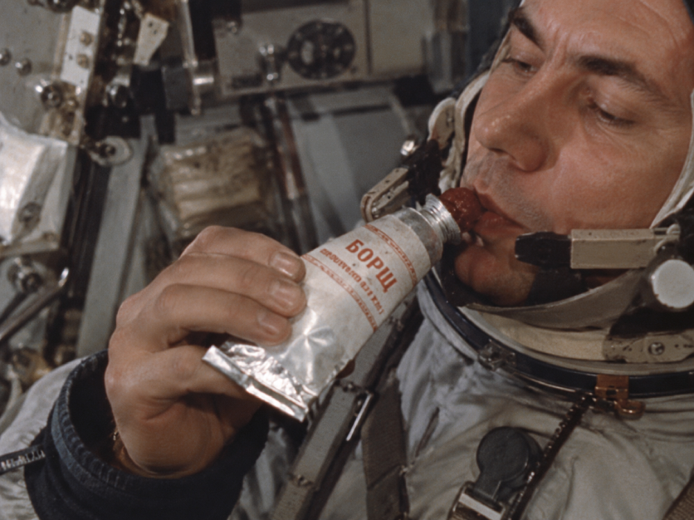A cosmonaut in a space suit eating borscht from a squeeze tube.