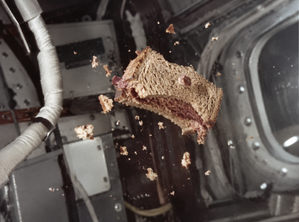 A corned beef sandwich floating in zero gravity inside a spacecraft, surrounded by loose bread crumbs.