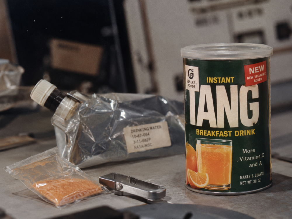 A container of Tang breakfast drink, a sealed pouch of orange powder, and a foil drinking water bag labeled NASA-MSC.