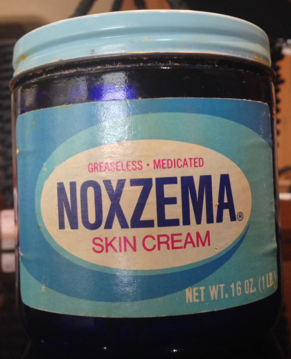 A jar of Noxzema Skin Cream with a light blue lid and a label reading “Greaseless Medicated Noxzema Skin Cream, Net Wt. 16 oz.”
