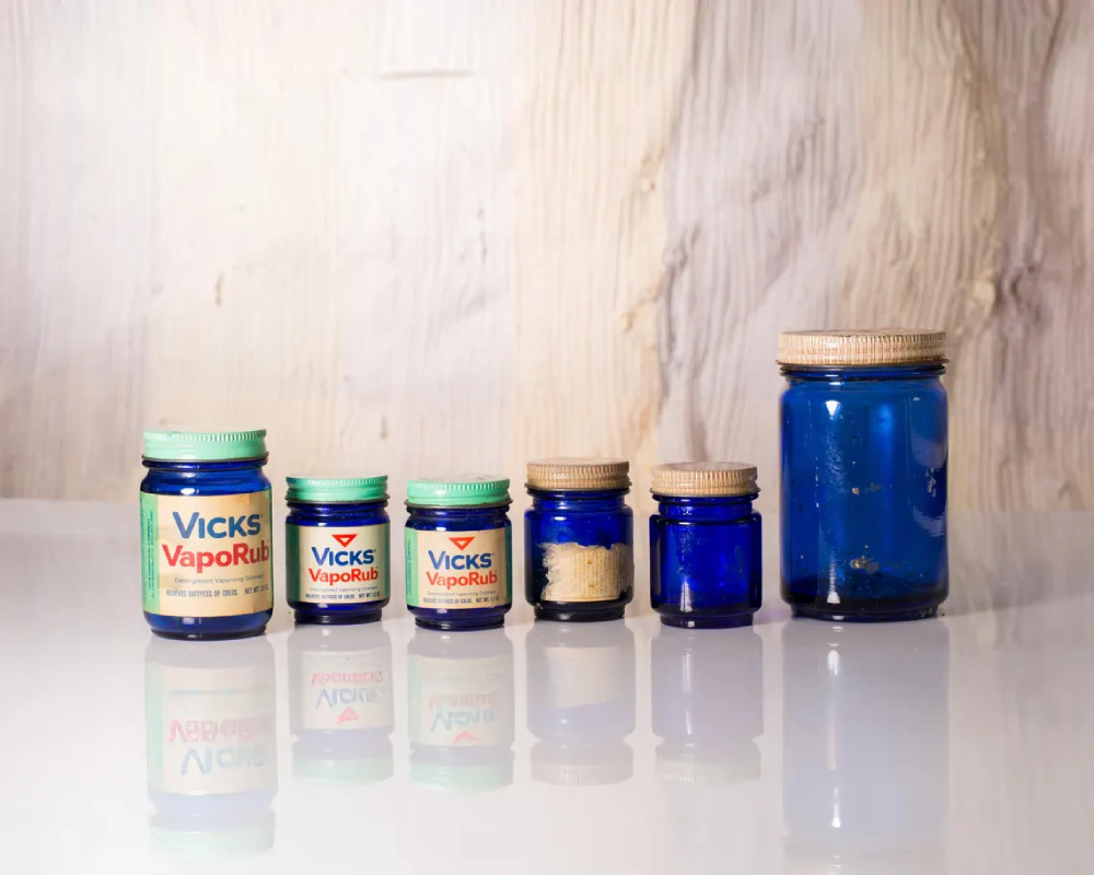 Six vintage blue glass Vicks VapoRub jars of varying sizes arranged in a row.