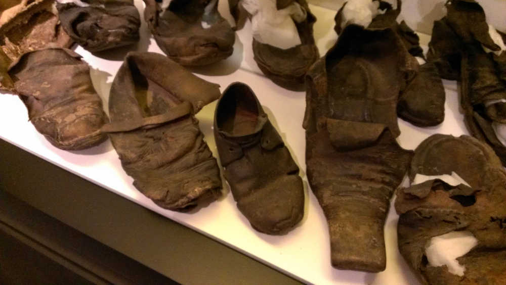 A collection of aged, worn leather historical shoes displayed on a white surface.