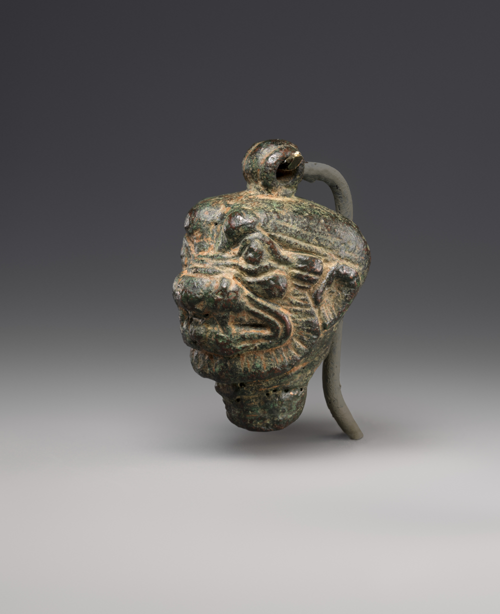 An ancient bronze bell shaped like a snarling creature’s head with a loop at the top for suspension.
