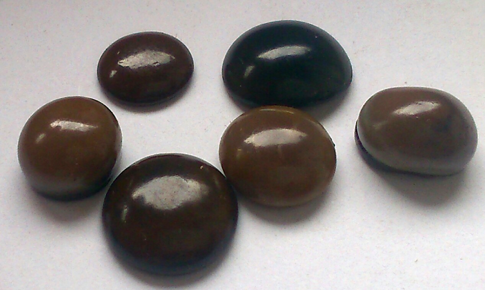 Six smooth, round, brown and black candies arranged on a white surface.