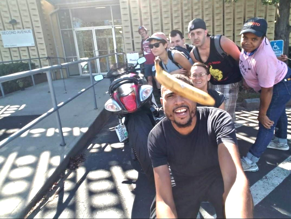 A group of people posing for a selfie with a motorcycle, with a banana held in the foreground.