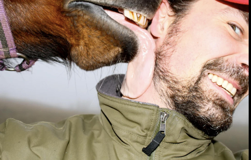 A horse licks the cheek of a smiling man.