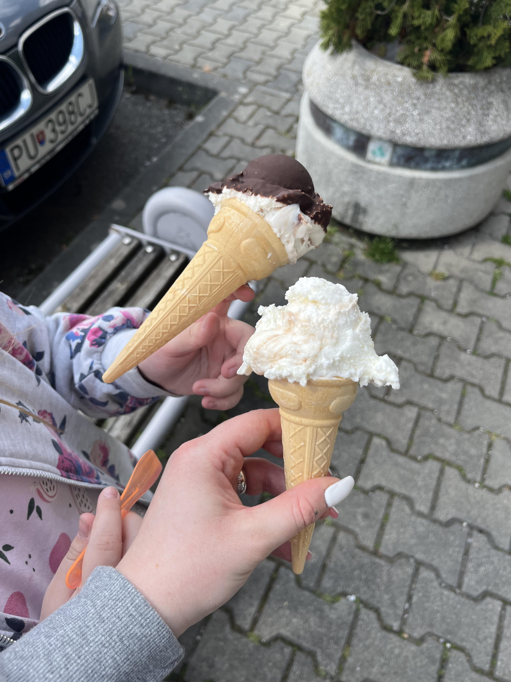 Two hands holding ice cream cones, one with a chocolate-dipped scoop and the other with a plain white scoop.