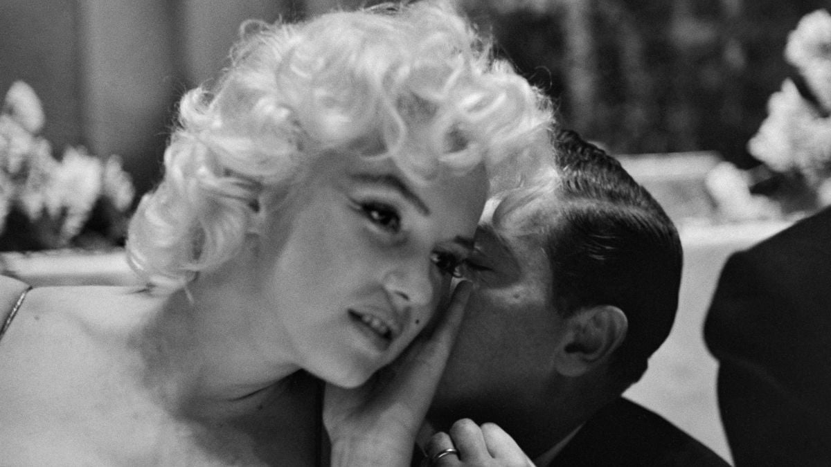 Marilyn Monroe listening as a man whispers in her ear.