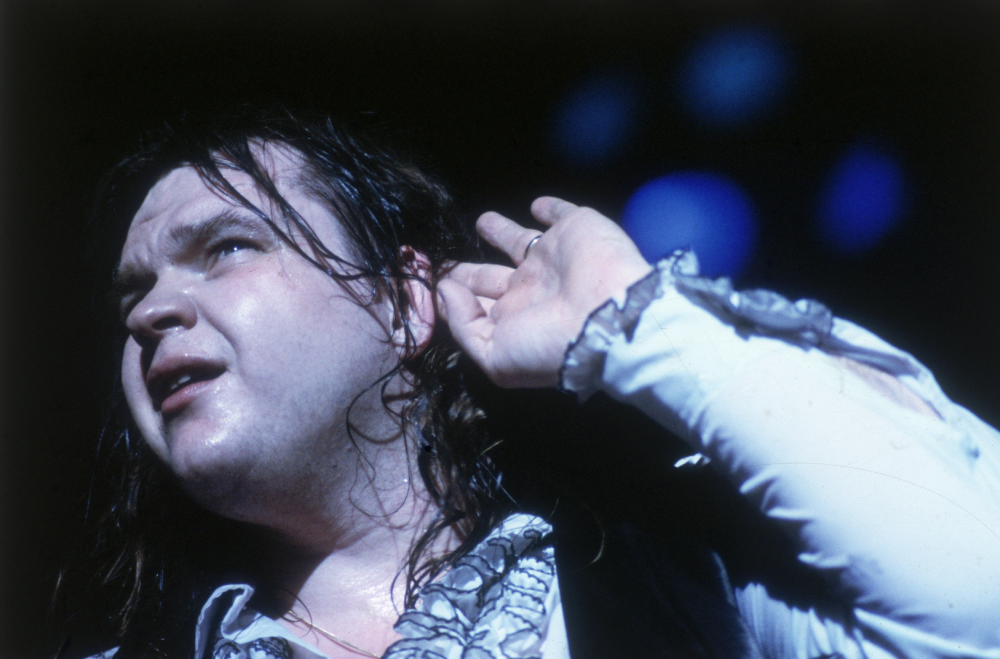 Meat Loaf performing on stage with his hand cupped to his ear.