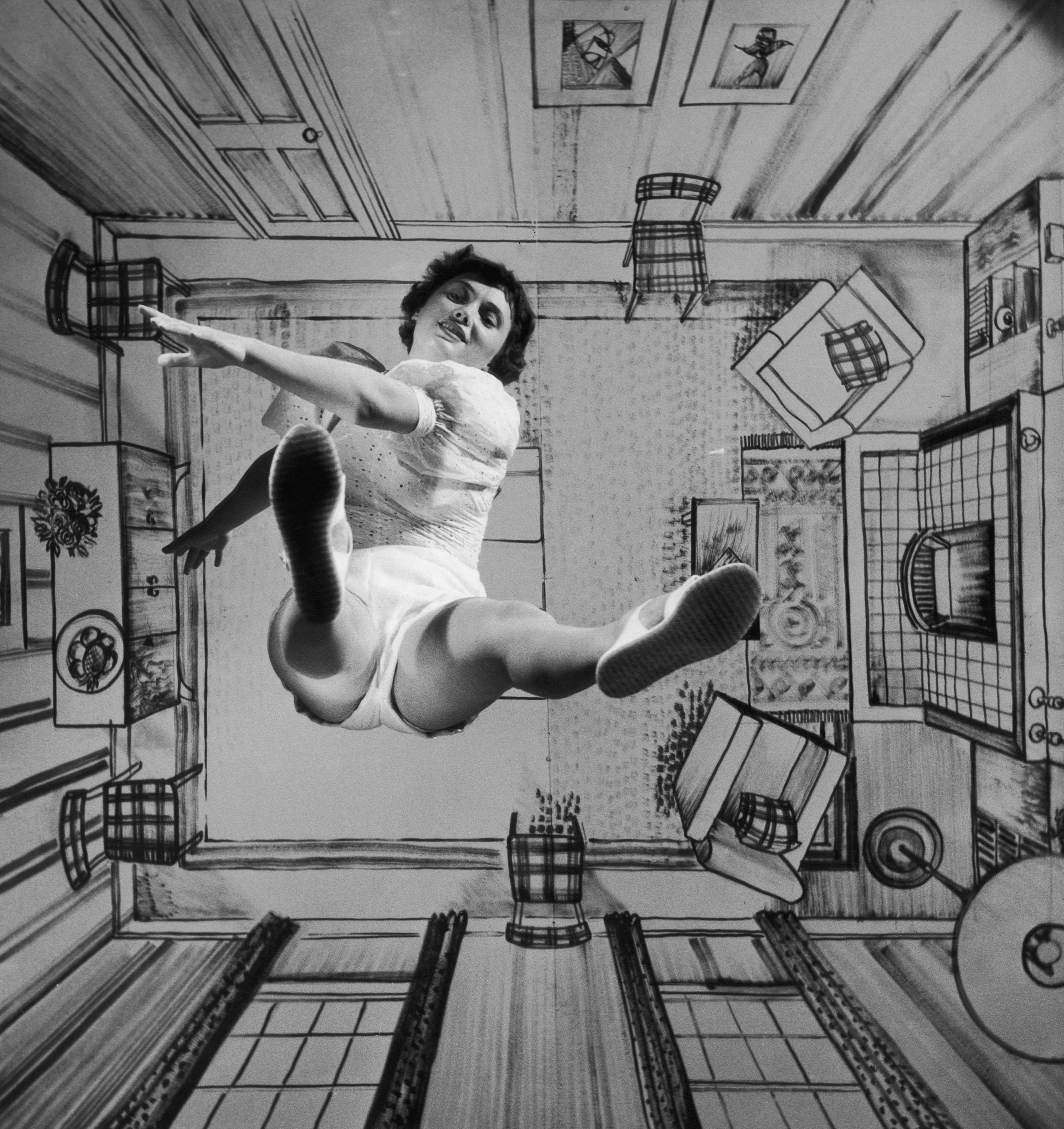A woman in shorts and a top jumps in front of a floor-to-ceiling illustration of a room interior, creating the illusion that she is falling through the scene.