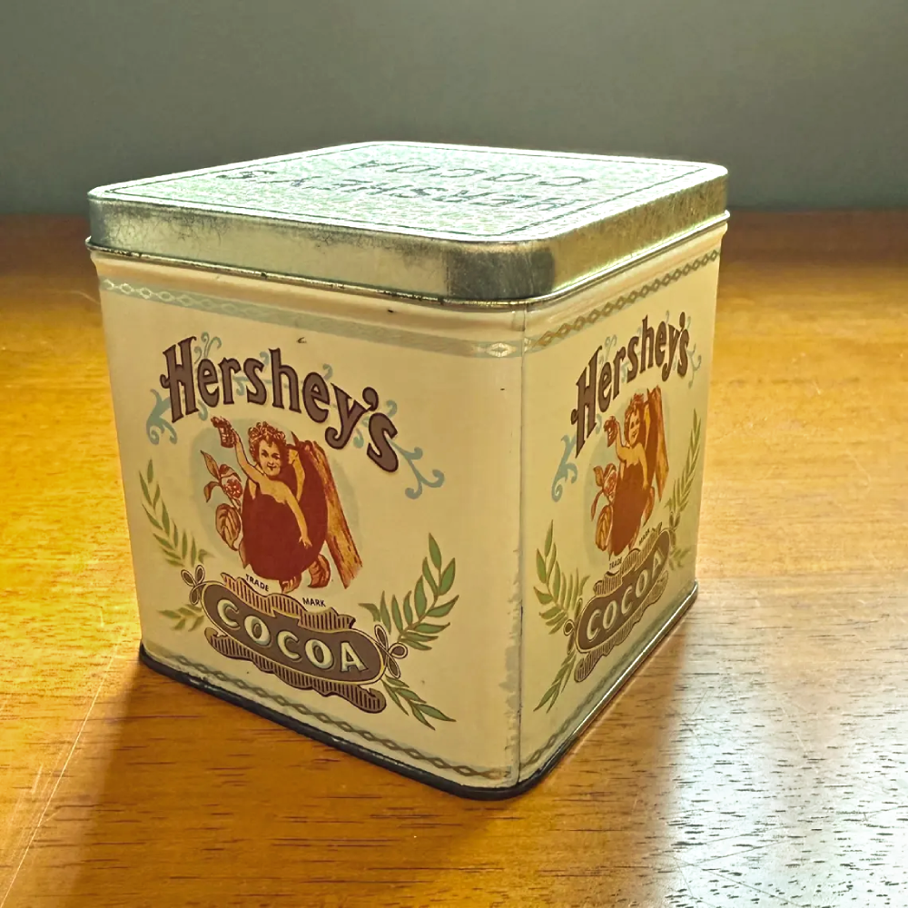 Vintage Hershey’s Cocoa square metal tin with a cherub graphic on the front and side.