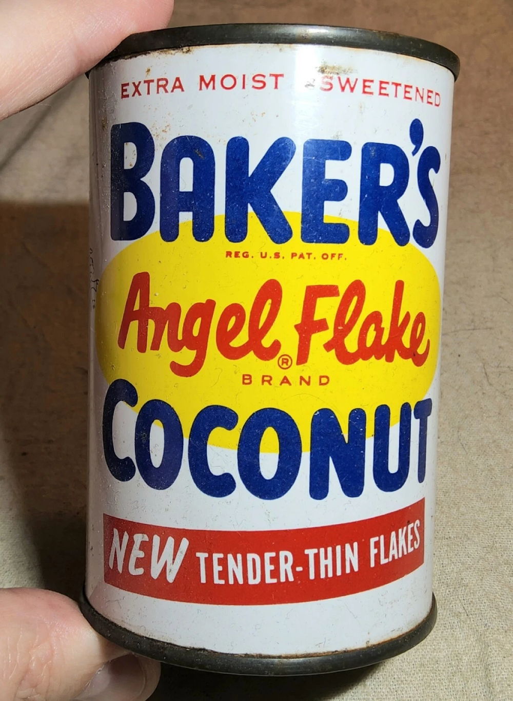 A vintage can of Baker’s Angel Flake Coconut with a white, blue, and yellow label that reads “Extra Moist Sweetened” and “New Tender-Thin Flakes.”