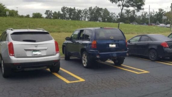 A dark blue SUV parked crookedly across two parking spaces in a lot.