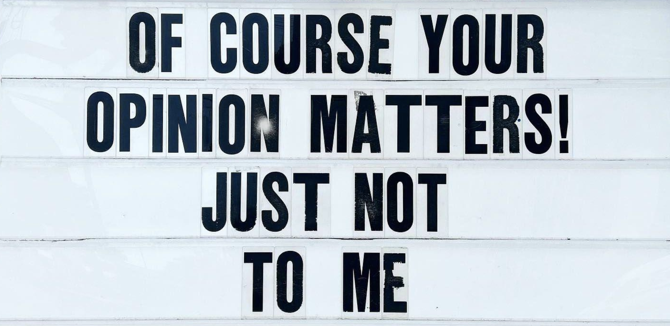 A sign with black lettering that reads: “OF COURSE YOUR OPINION MATTERS! JUST NOT TO ME.”