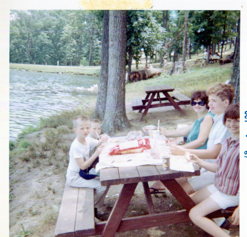 A family sits at a picnic table by a lake eating a meal.