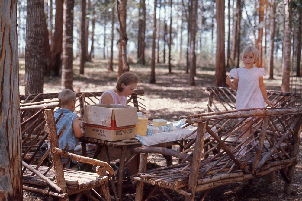 A woman and two children sit at a rustic twig table in a wooded area, with a Ryvita crisp rye bread box on the table.