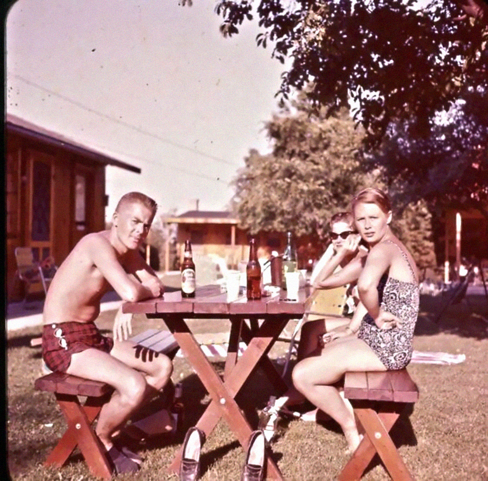 Three people sitting at a wooden picnic table outdoors on a sunny day.