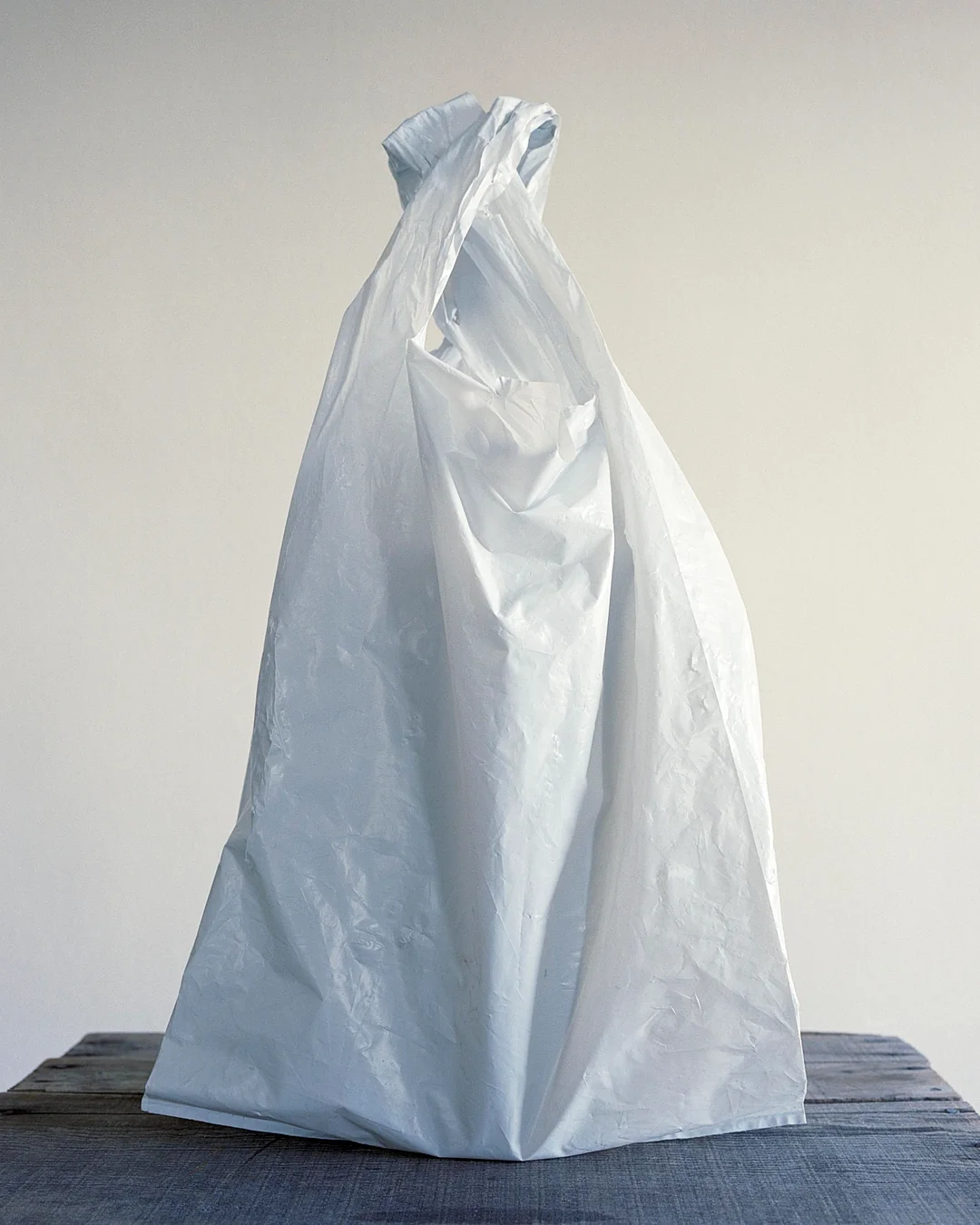 A white plastic grocery bag standing upright on a wooden surface.